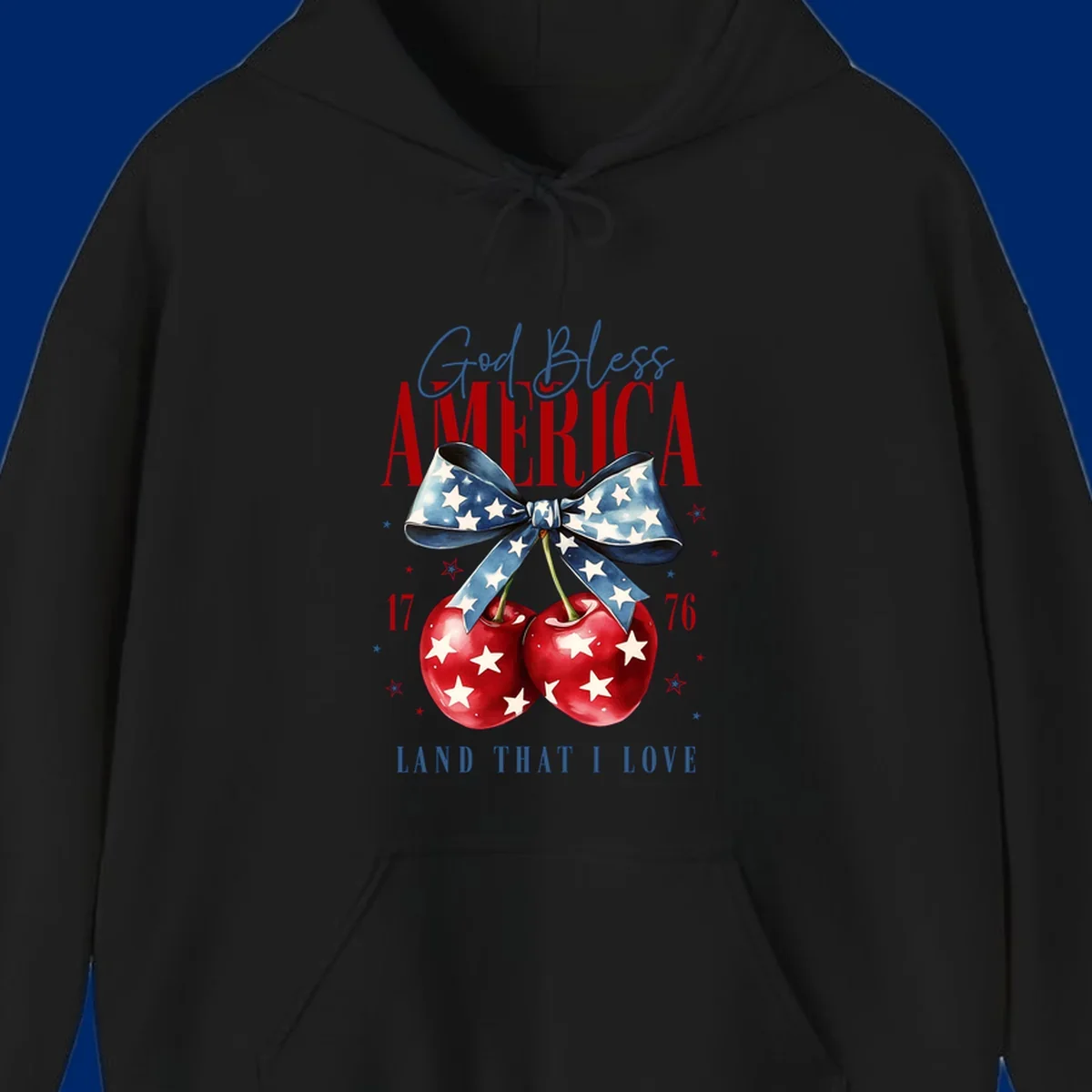 A patriotic design featuring 'God Bless AMERICA' and 'LAND THAT I LOVE' with a blue star-spangled bow, two red star-covered cherries, and the numbers '17' and '76'. god-bless-america-cherries.