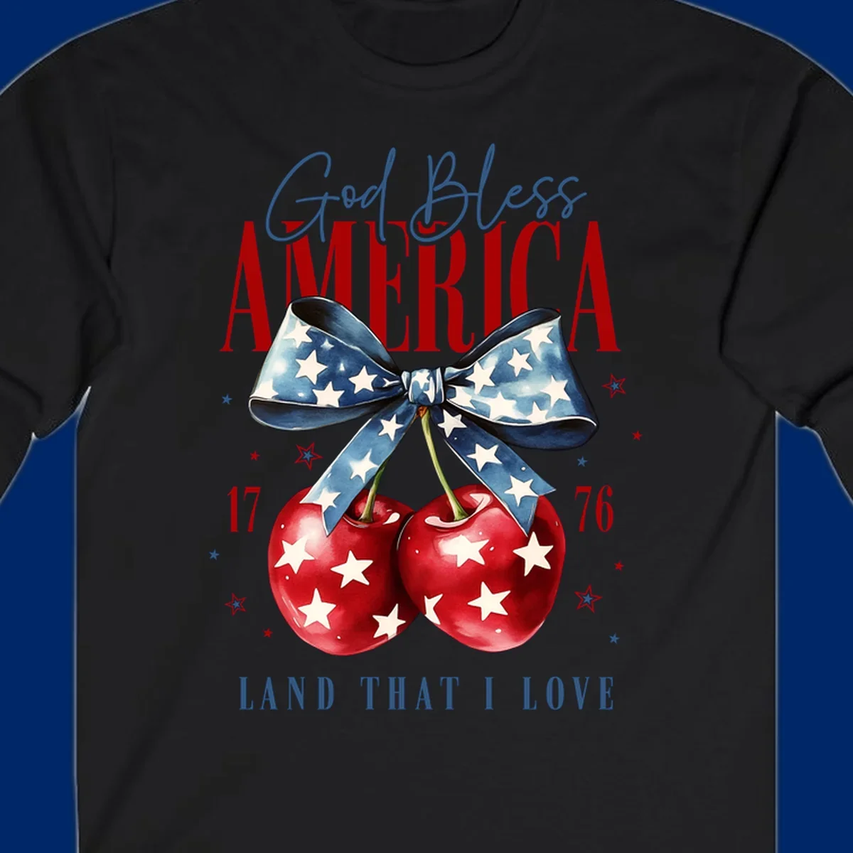 A patriotic design featuring 'God Bless AMERICA' and 'LAND THAT I LOVE' with a blue star-spangled bow, two red star-covered cherries, and the numbers '17' and '76'. god-bless-america-cherries.