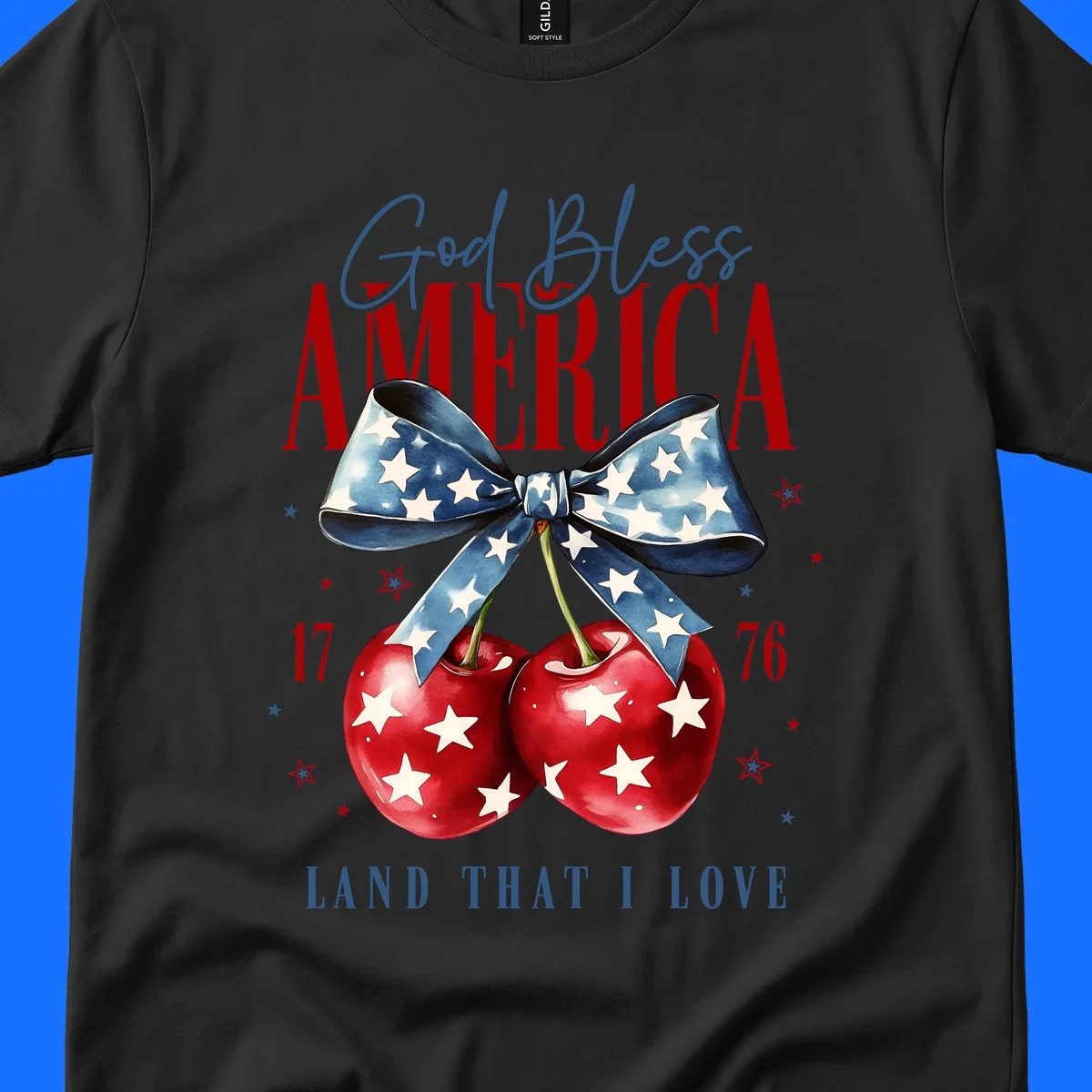 A patriotic design featuring 'God Bless AMERICA' and 'LAND THAT I LOVE' with a blue star-spangled bow, two red star-covered cherries, and the numbers '17' and '76'. god-bless-america-cherries.