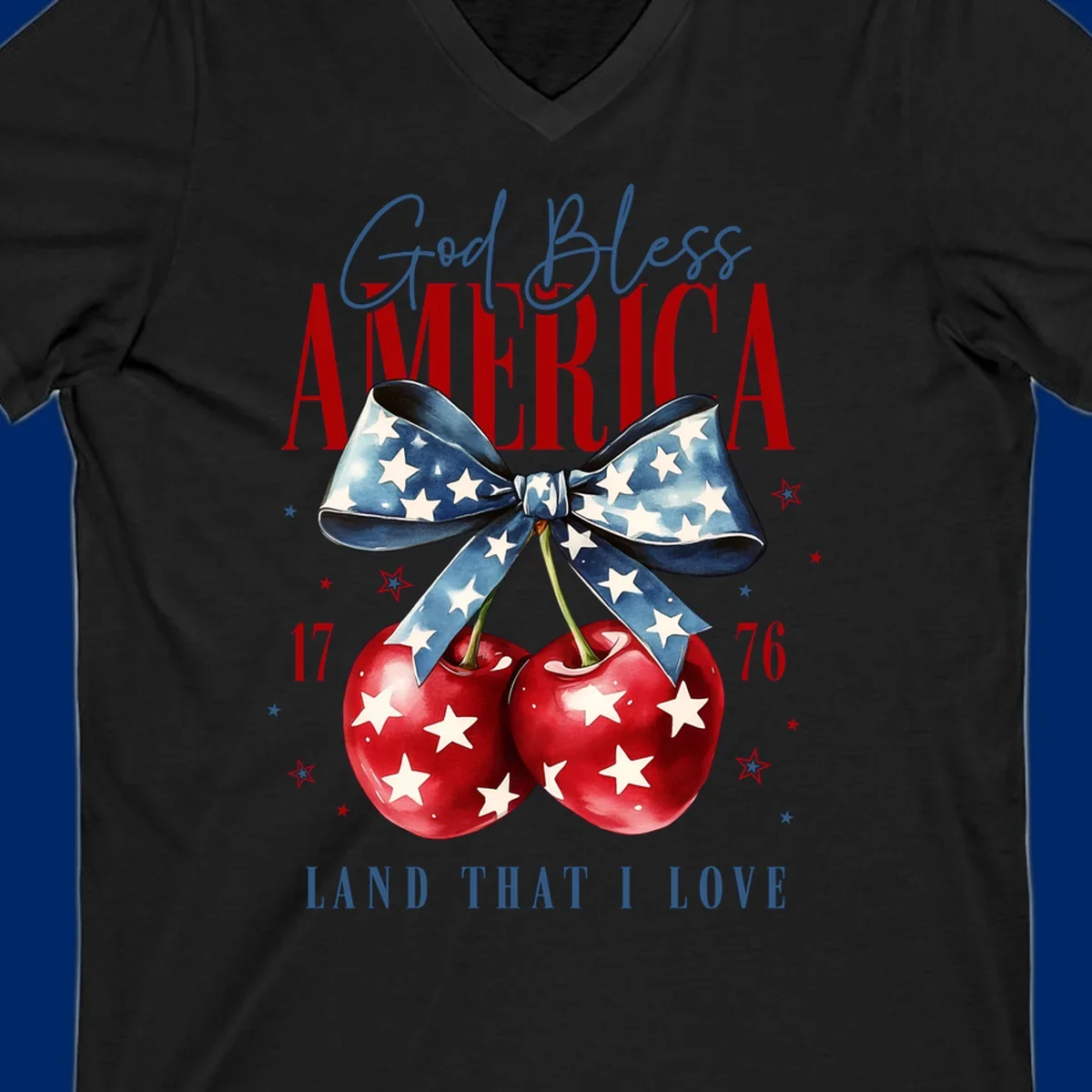 A patriotic design featuring 'God Bless AMERICA' and 'LAND THAT I LOVE' with a blue star-spangled bow, two red star-covered cherries, and the numbers '17' and '76'. god-bless-america-cherries.