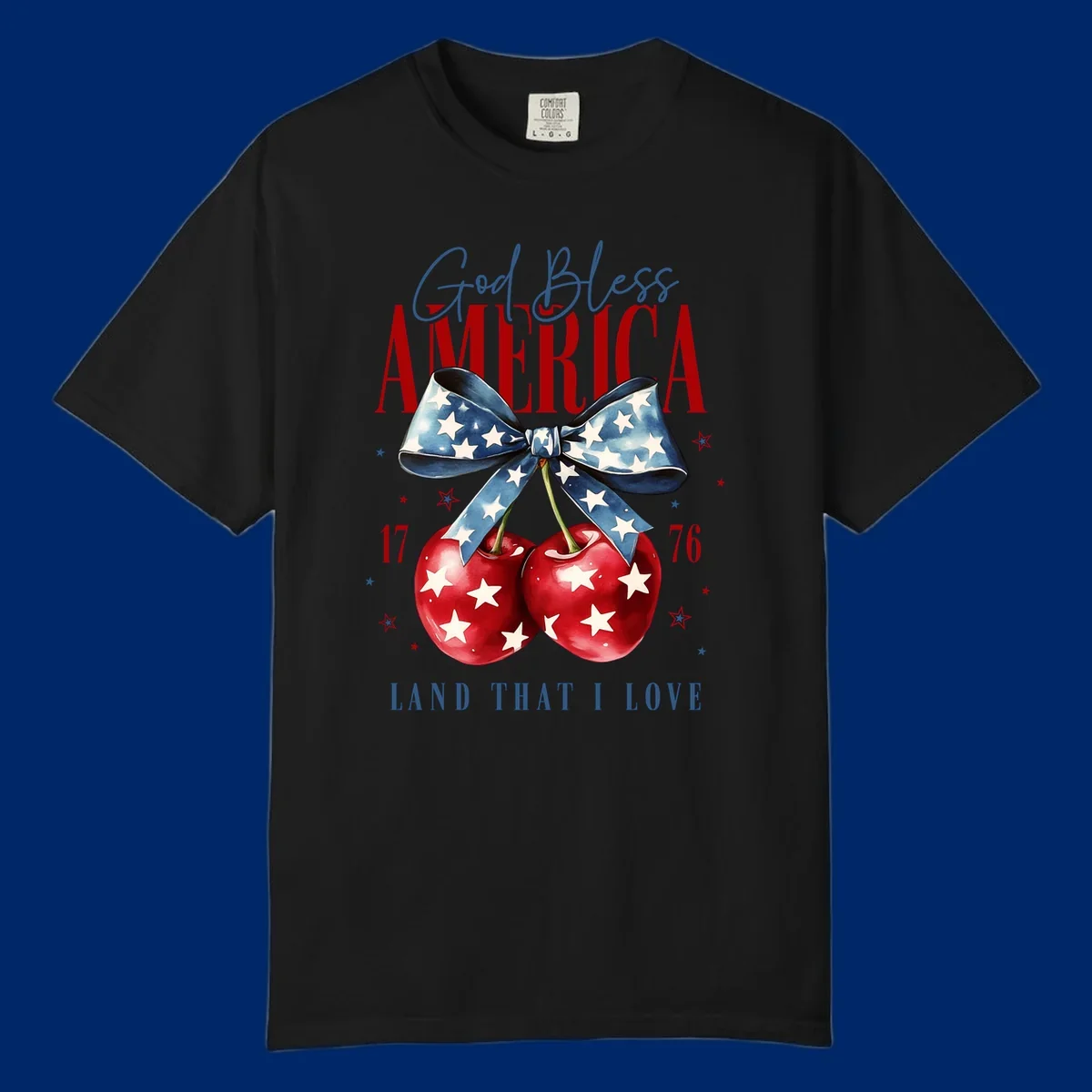 A patriotic design featuring 'God Bless AMERICA' and 'LAND THAT I LOVE' with a blue star-spangled bow, two red star-covered cherries, and the numbers '17' and '76'. god-bless-america-cherries.