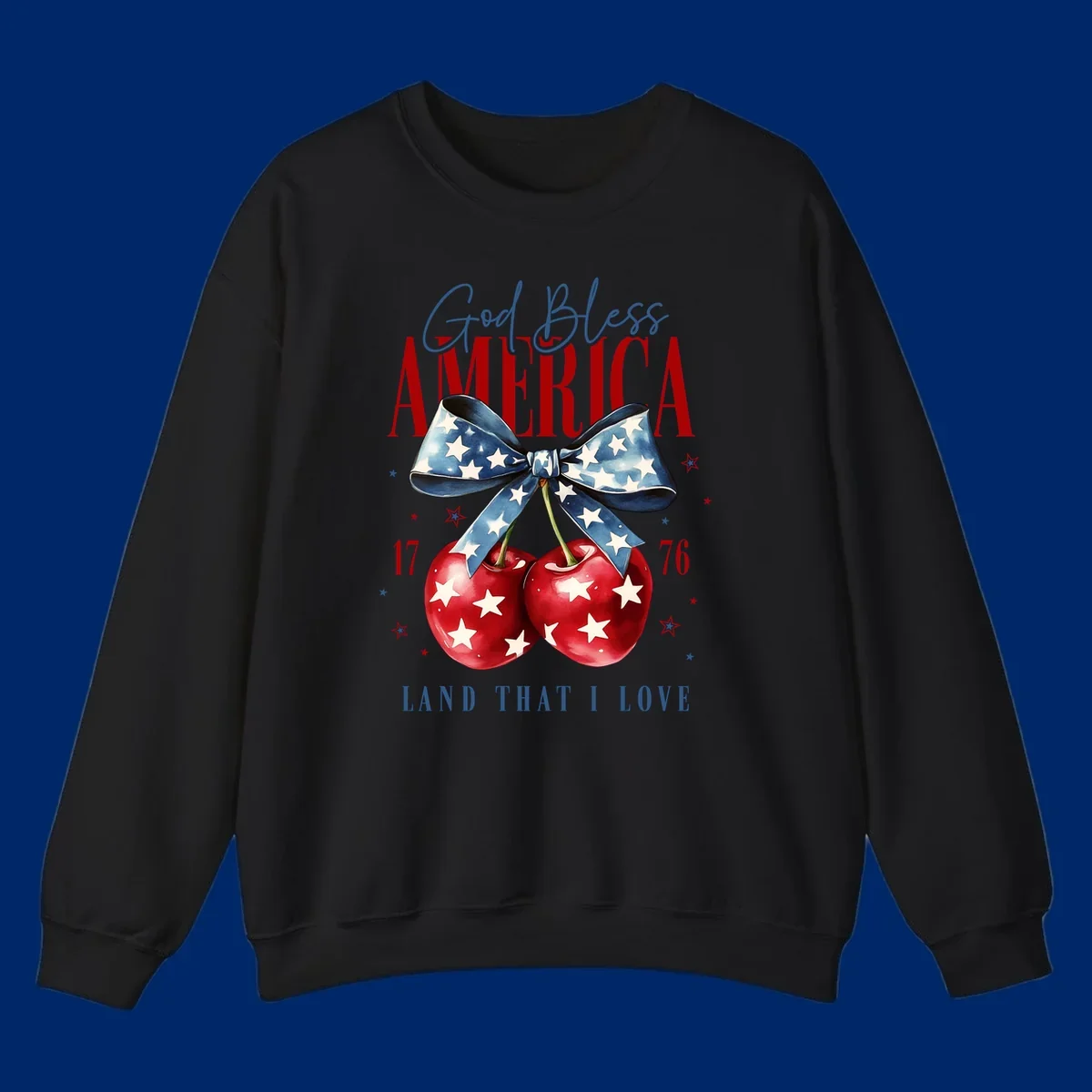 A patriotic design featuring 'God Bless AMERICA' and 'LAND THAT I LOVE' with a blue star-spangled bow, two red star-covered cherries, and the numbers '17' and '76'. god-bless-america-cherries.