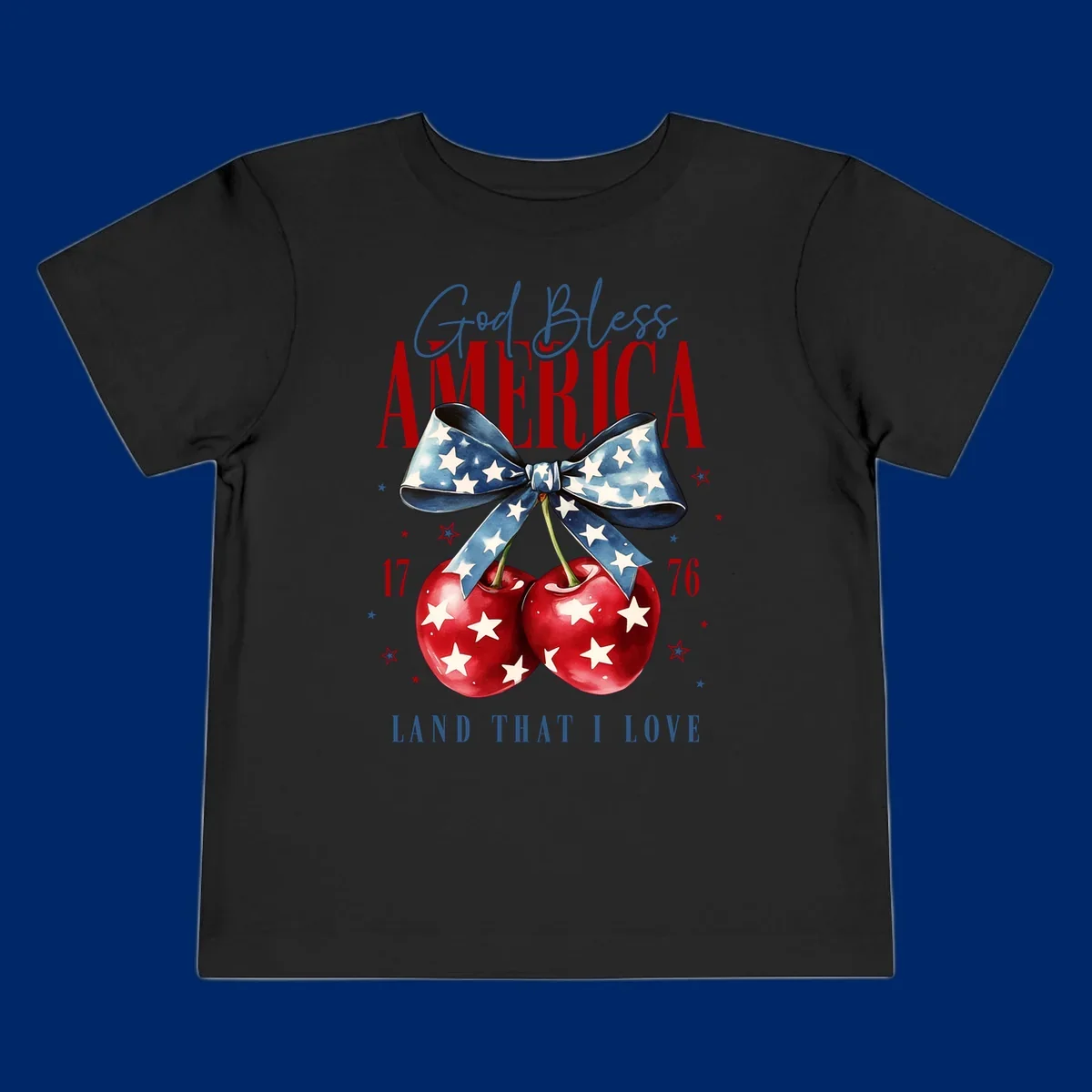 A patriotic design featuring 'God Bless AMERICA' and 'LAND THAT I LOVE' with a blue star-spangled bow, two red star-covered cherries, and the numbers '17' and '76'. god-bless-america-cherries.