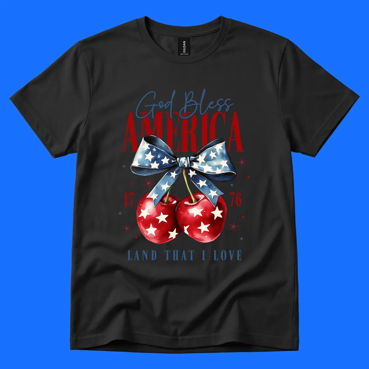 A patriotic design featuring 'God Bless AMERICA' and 'LAND THAT I LOVE' with a blue star-spangled bow, two red star-covered cherries, and the numbers '17' and '76'. god-bless-america-cherries.
