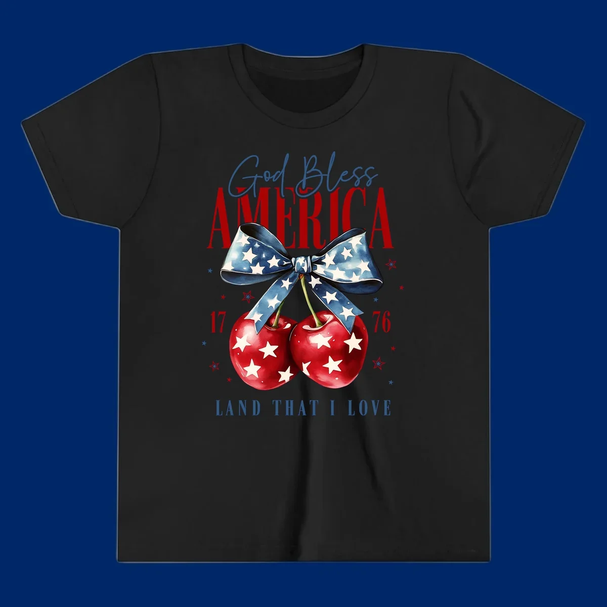 A patriotic design featuring 'God Bless AMERICA' and 'LAND THAT I LOVE' with a blue star-spangled bow, two red star-covered cherries, and the numbers '17' and '76'. god-bless-america-cherries.