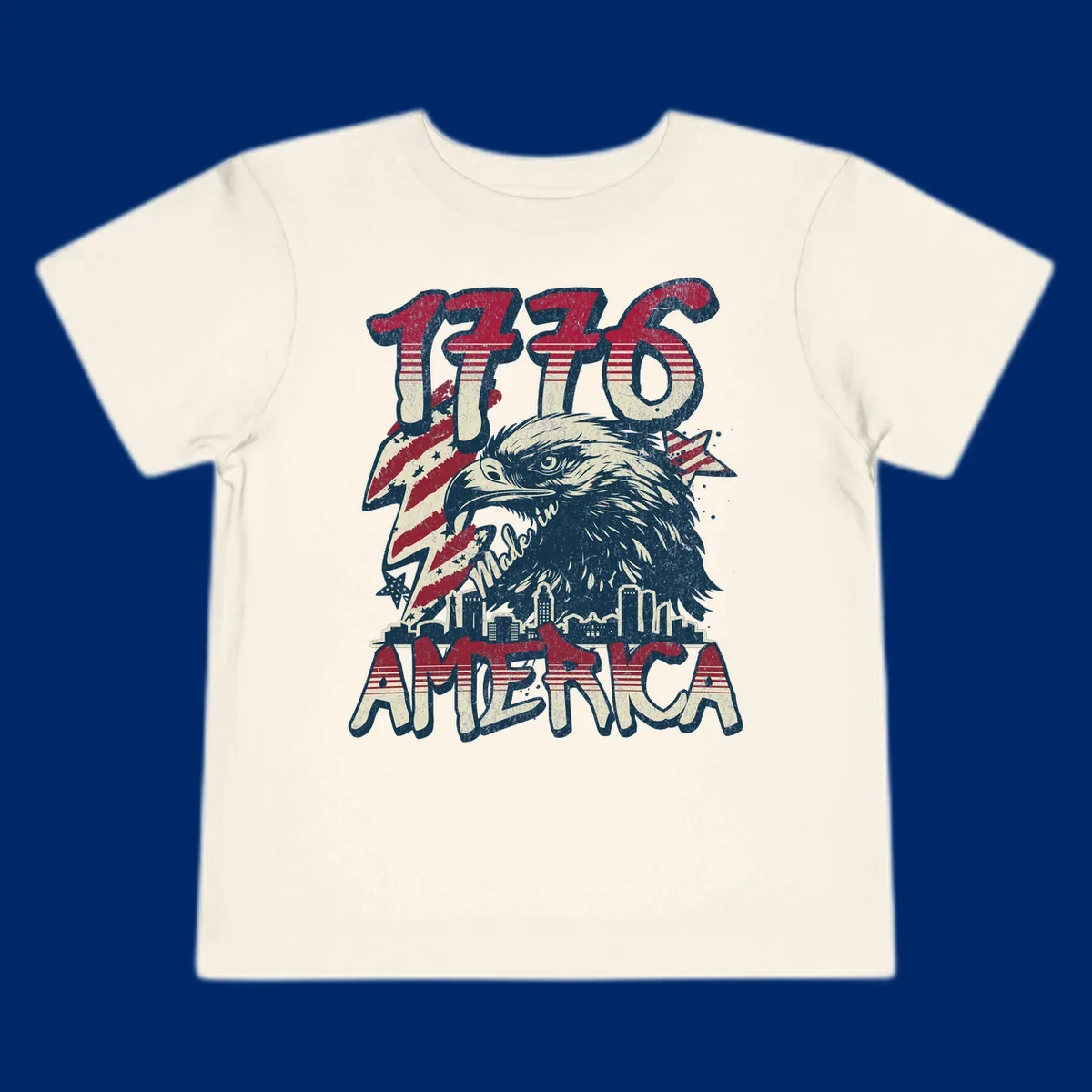 Vintage 1776 Made in America design with a bald eagle, city skyline, and American flag pattern. Features distressed red, cream, and navy colors.