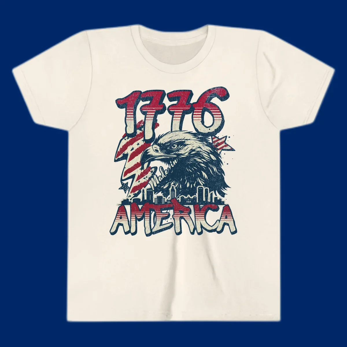 Vintage 1776 Made in America design with a bald eagle, city skyline, and American flag pattern. Features distressed red, cream, and navy colors.