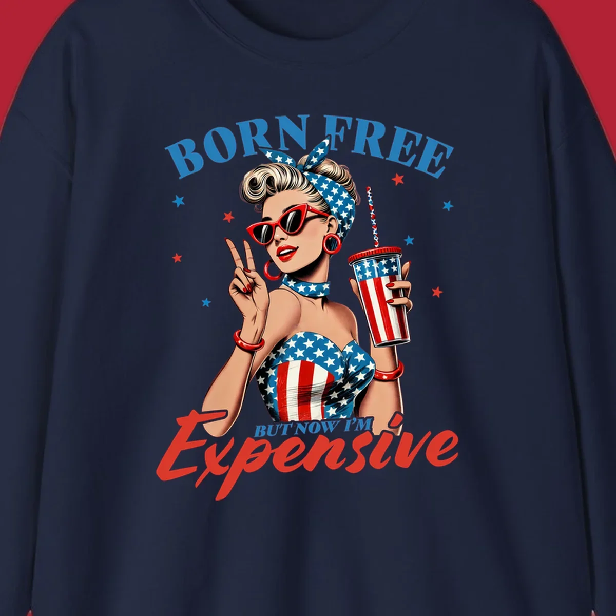 A vintage pin-up girl with a patriotic outfit and cup, making a peace sign, with the text "Born Free But Now I'm Expensive". This born-free-expensive-pinup design is surrounded by stars.