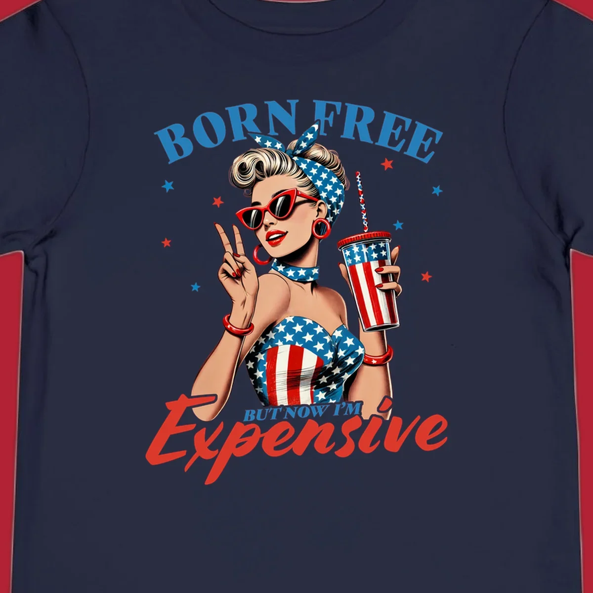 A vintage pin-up girl with a patriotic outfit and cup, making a peace sign, with the text "Born Free But Now I'm Expensive". This born-free-expensive-pinup design is surrounded by stars.
