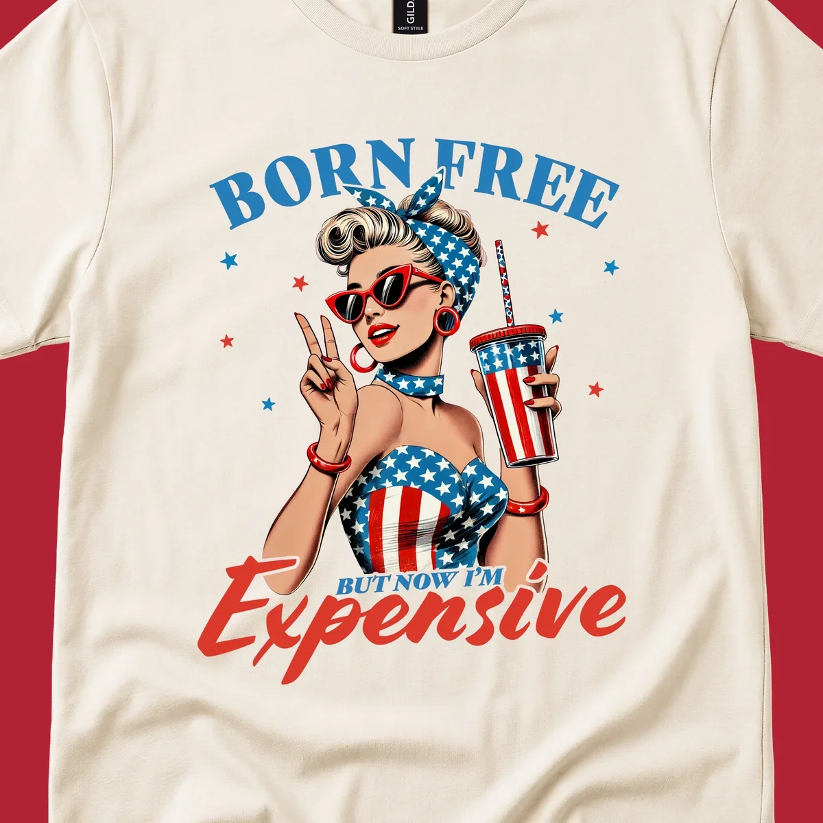 A vintage pin-up girl with a patriotic outfit and cup, making a peace sign, with the text "Born Free But Now I'm Expensive". This born-free-expensive-pinup design is surrounded by stars.