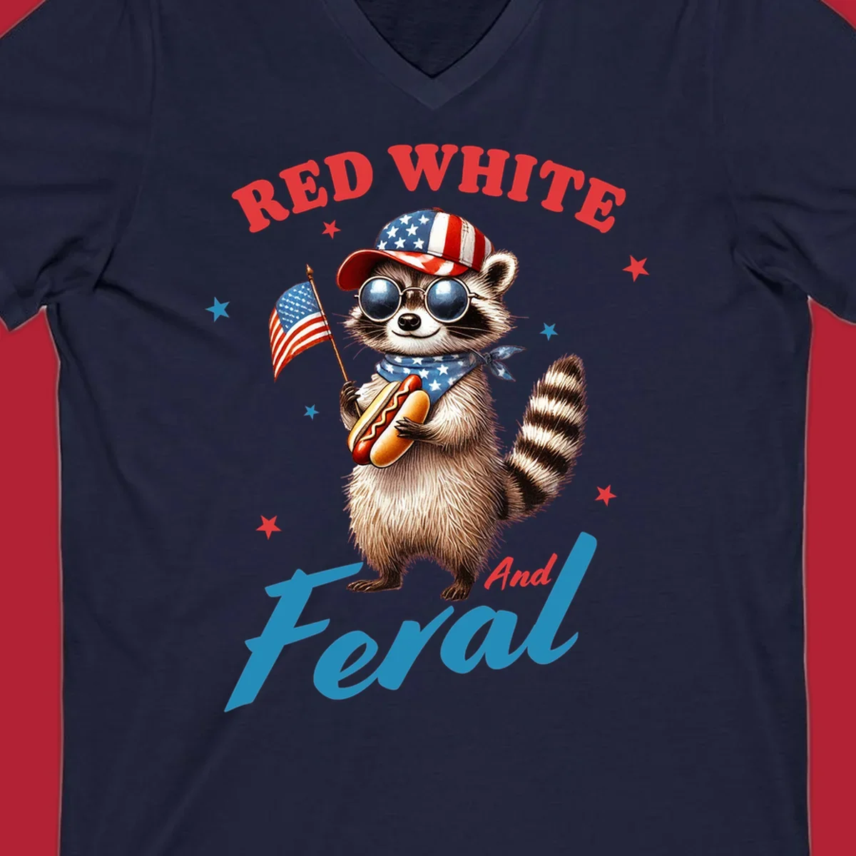 A cartoon raccoon wearing a patriotic hat and bandana, holding an American flag and a hot dog, with 'Red White And Feral' text. This is a red-white-feral-raccoon design.