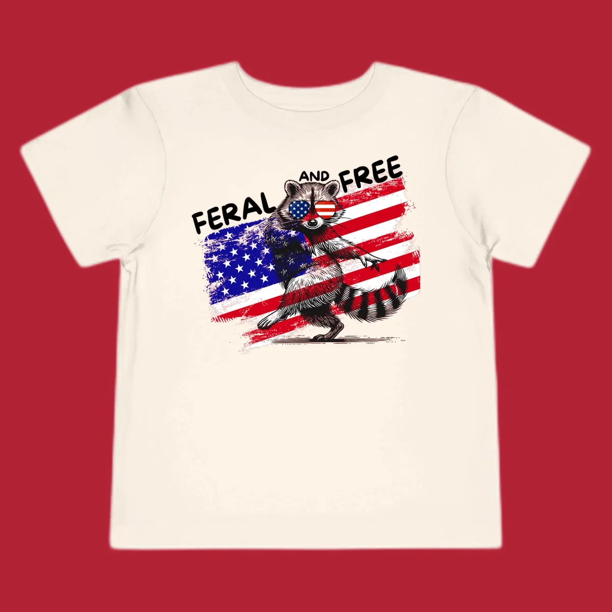 A standing raccoon with an American flag design and USA flag sunglasses, with the text 'FERAL AND FREE'. feral-free-raccoon-flag.