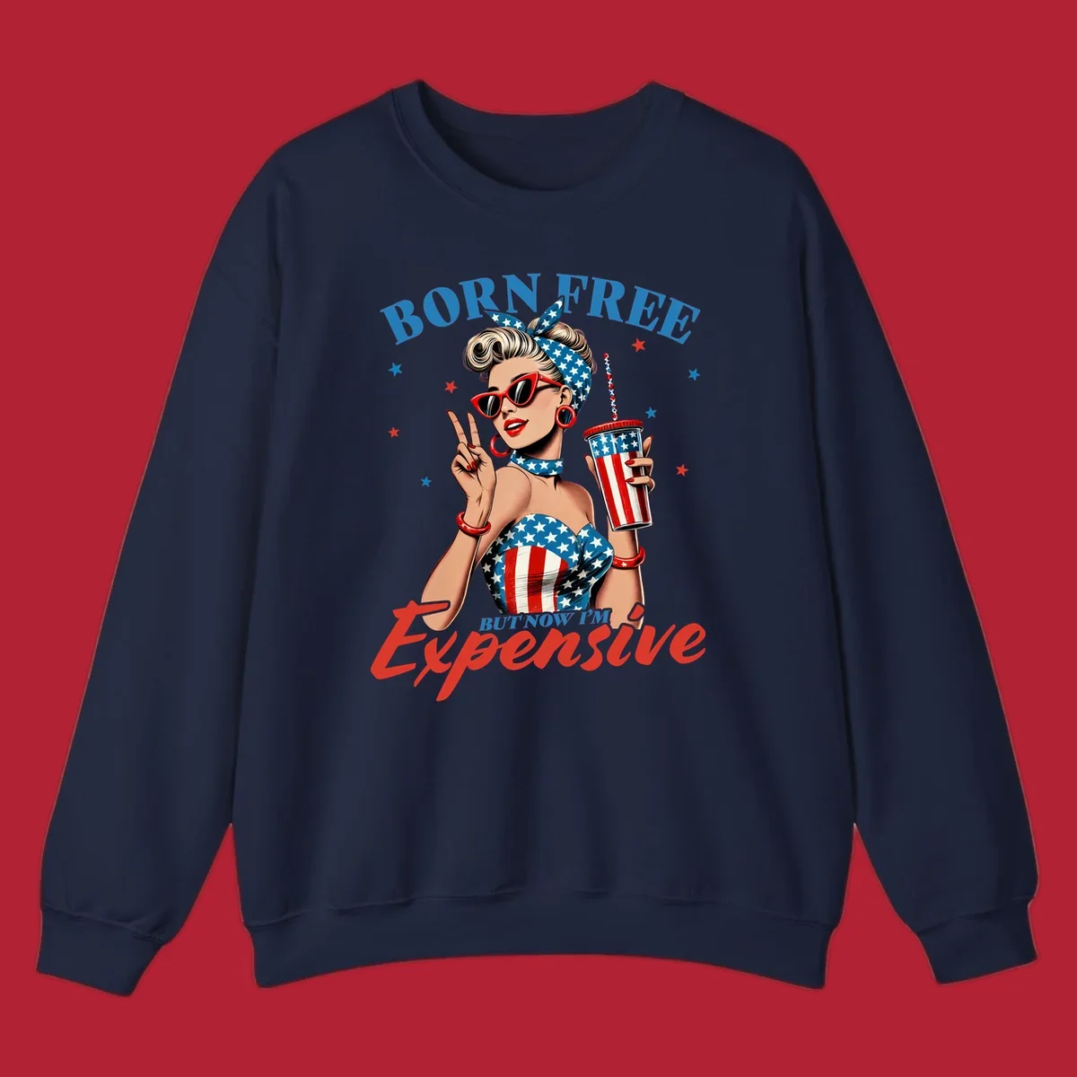 A vintage pin-up girl with a patriotic outfit and cup, making a peace sign, with the text "Born Free But Now I'm Expensive". This born-free-expensive-pinup design is surrounded by stars.