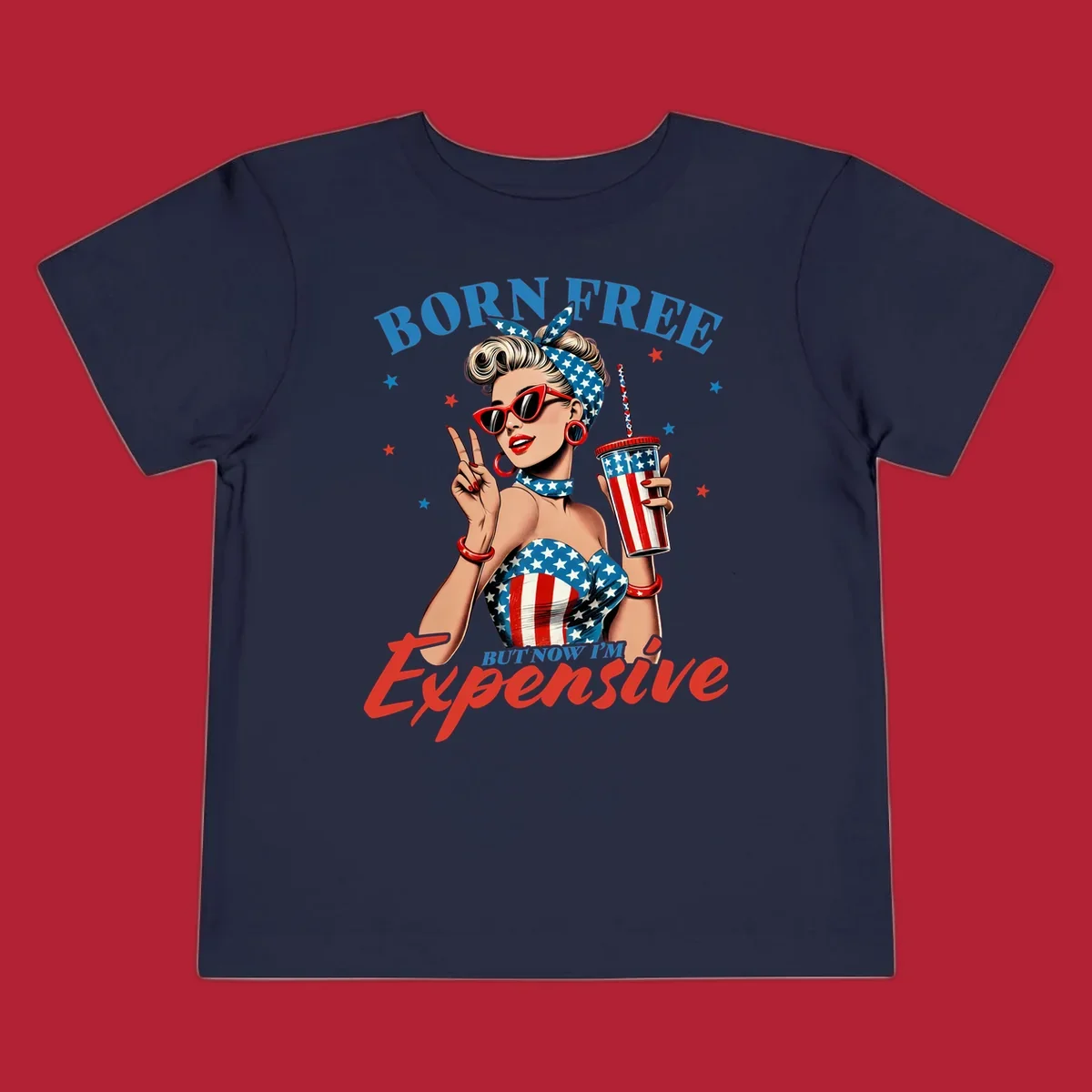 A vintage pin-up girl with a patriotic outfit and cup, making a peace sign, with the text "Born Free But Now I'm Expensive". This born-free-expensive-pinup design is surrounded by stars.