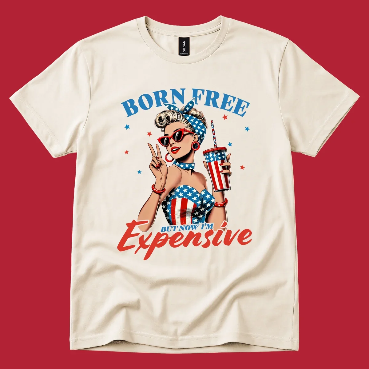 A vintage pin-up girl with a patriotic outfit and cup, making a peace sign, with the text "Born Free But Now I'm Expensive". This born-free-expensive-pinup design is surrounded by stars.