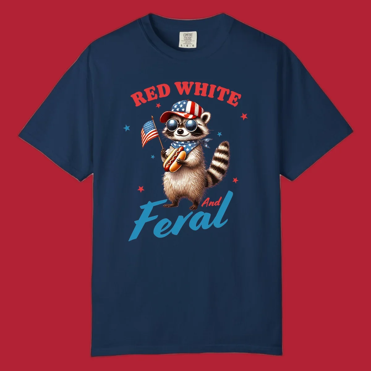 A cartoon raccoon wearing a patriotic hat and bandana, holding an American flag and a hot dog, with 'Red White And Feral' text. This is a red-white-feral-raccoon design.