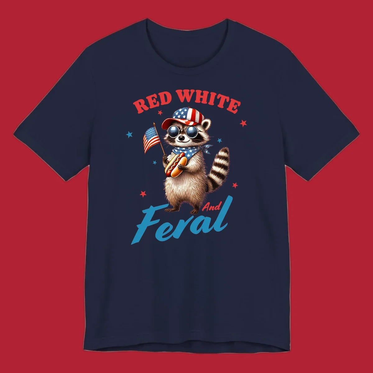 A cartoon raccoon wearing a patriotic hat and bandana, holding an American flag and a hot dog, with 'Red White And Feral' text. This is a red-white-feral-raccoon design.