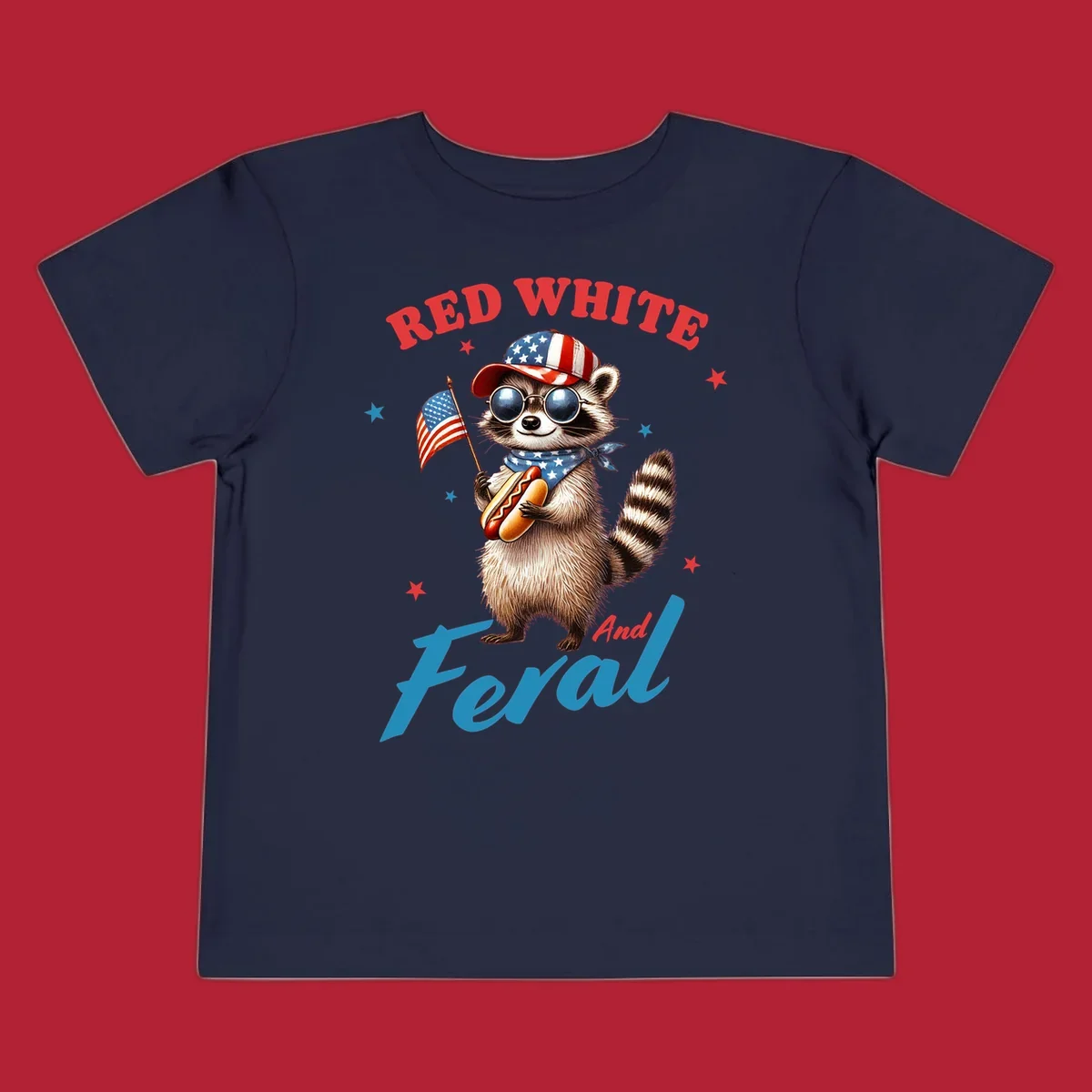 A cartoon raccoon wearing a patriotic hat and bandana, holding an American flag and a hot dog, with 'Red White And Feral' text. This is a red-white-feral-raccoon design.
