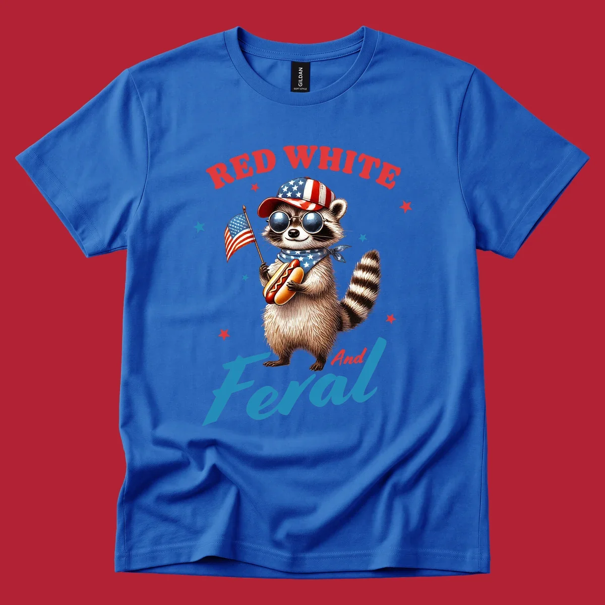 A cartoon raccoon wearing a patriotic hat and bandana, holding an American flag and a hot dog, with 'Red White And Feral' text. This is a red-white-feral-raccoon design.