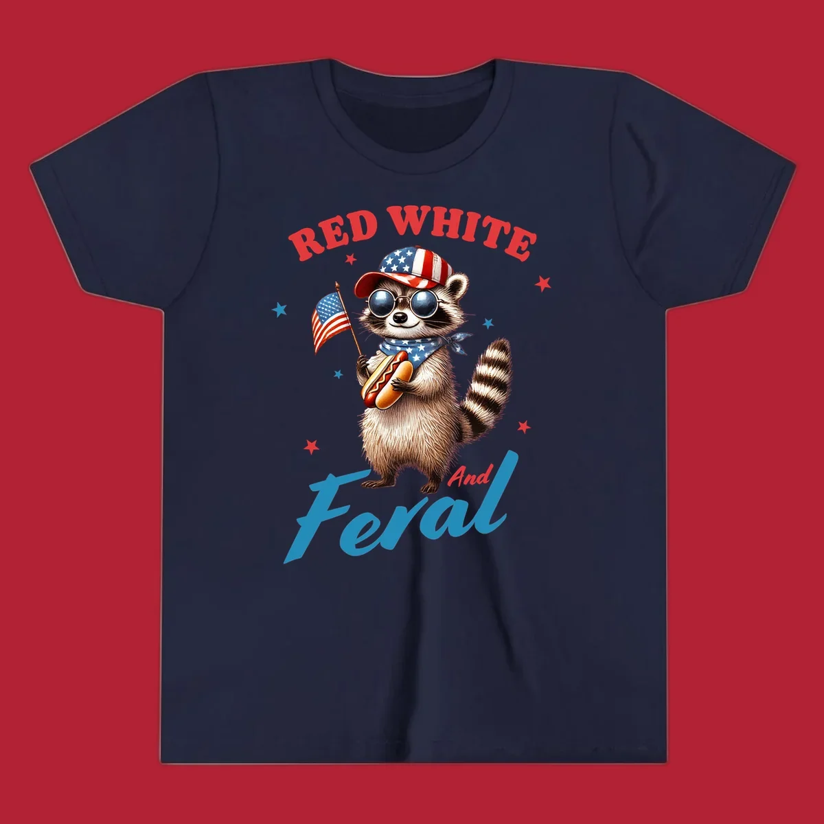 A cartoon raccoon wearing a patriotic hat and bandana, holding an American flag and a hot dog, with 'Red White And Feral' text. This is a red-white-feral-raccoon design.