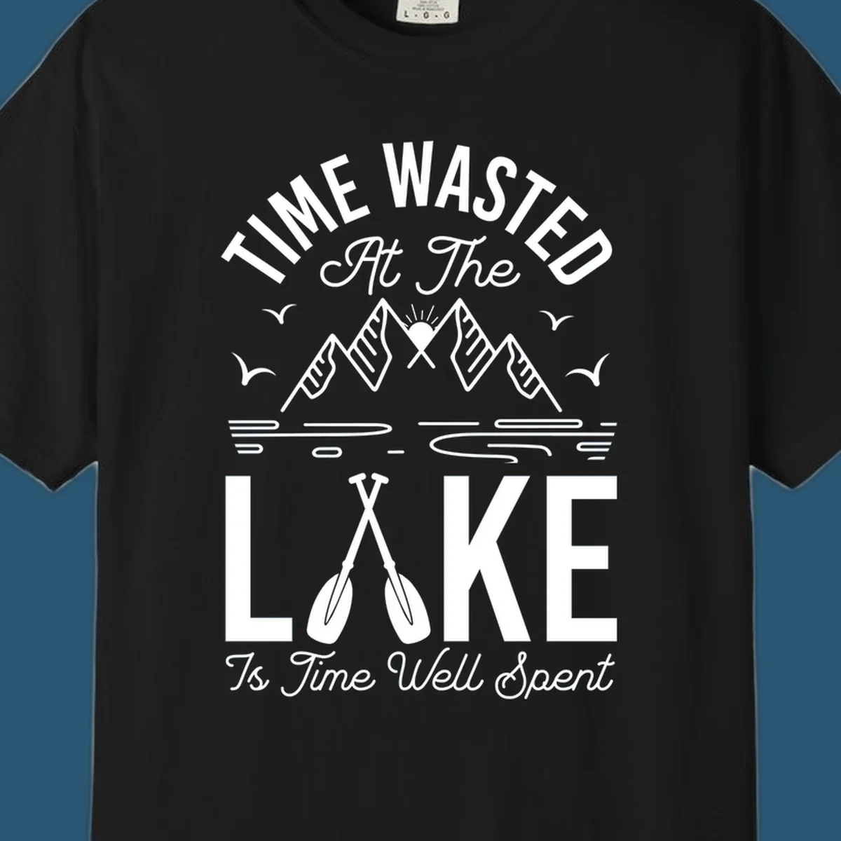 Illustration of mountains, sun, birds, and oars with text 'Time Wasted At The Lake Is Time Well Spent'.