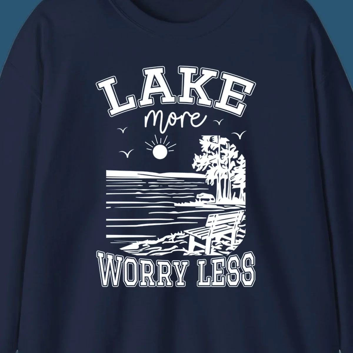 Lake More Worry Less scenic illustration with lake, trees, bench, and sun, white text on black, navy text on white.