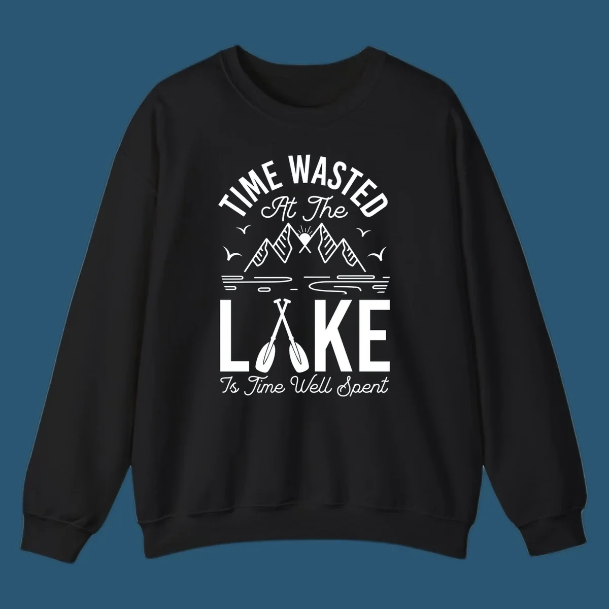 Illustration of mountains, sun, birds, and oars with text 'Time Wasted At The Lake Is Time Well Spent'.