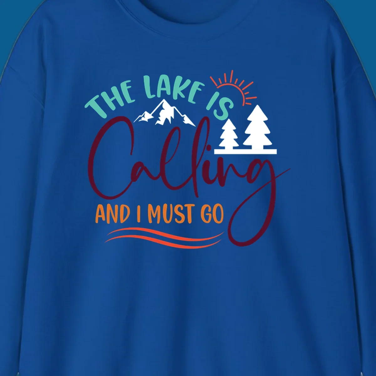 The Lake Is Calling And I Must Go nature graphic with mountains, trees, and sun rays.