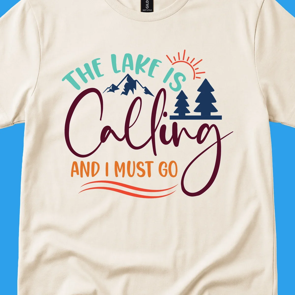 The Lake Is Calling And I Must Go nature graphic with mountains, trees, and sun rays.