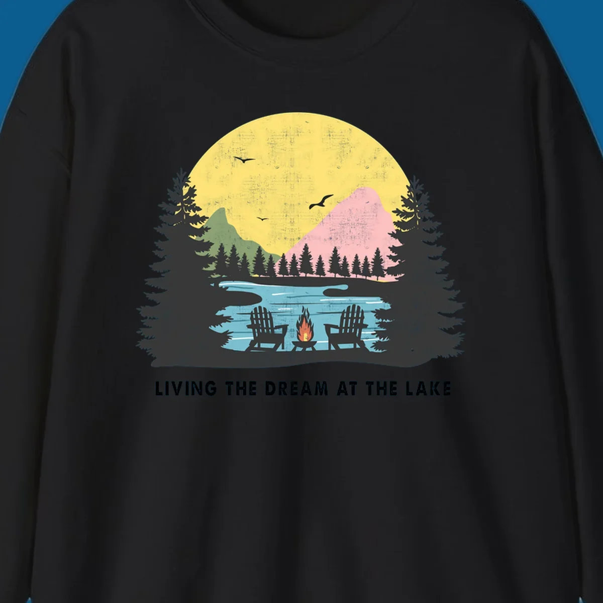 Lake life dream scene with Adirondack chairs, campfire, and sunset over mountains. Text: LIVING THE DREAM AT THE LAKE