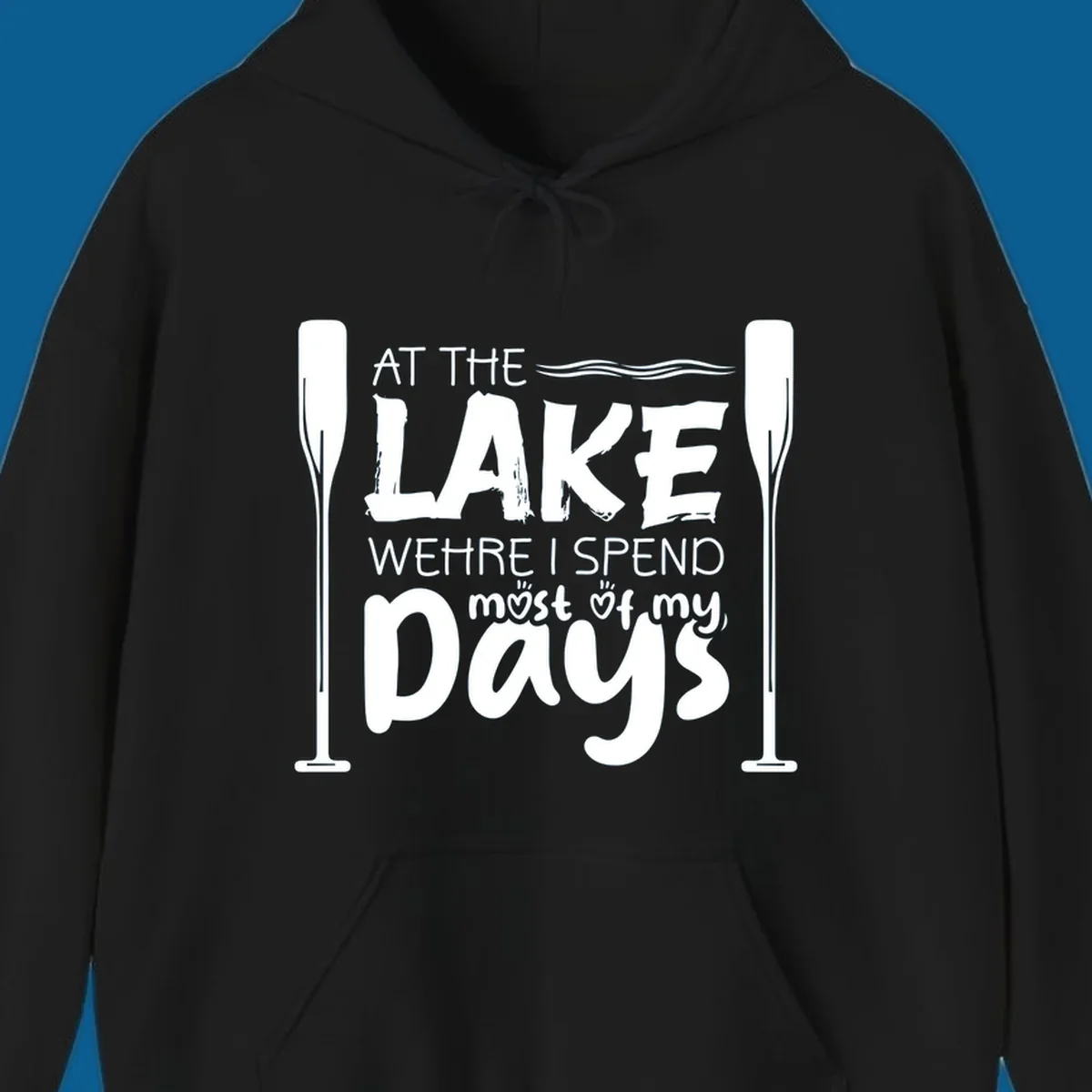 Text design "At The Lake Where I Spend Most Of My Days" with paddles and waves, lake-life-days concept.