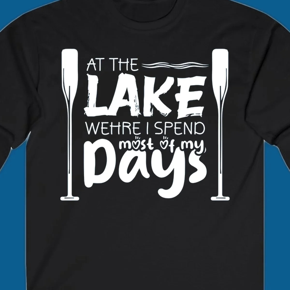 Text design "At The Lake Where I Spend Most Of My Days" with paddles and waves, lake-life-days concept.