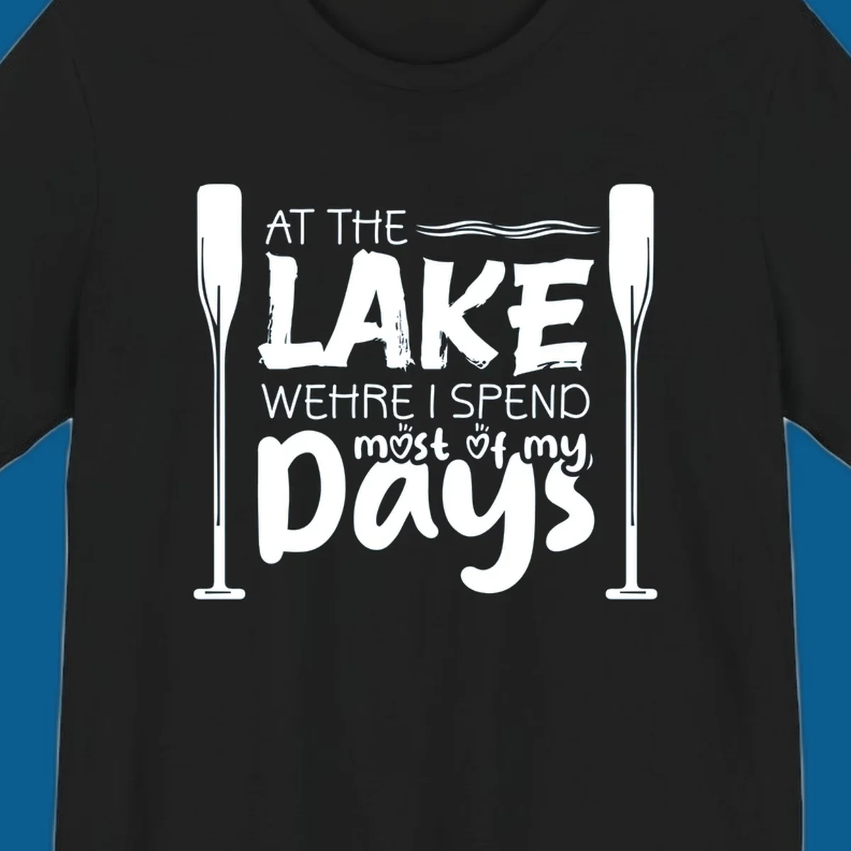 Text design "At The Lake Where I Spend Most Of My Days" with paddles and waves, lake-life-days concept.