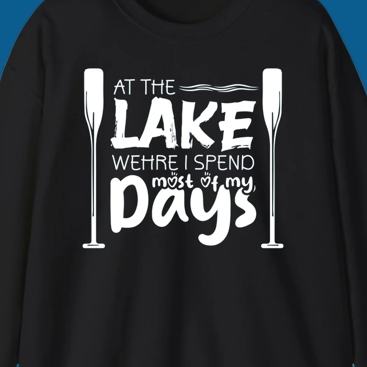 Text design "At The Lake Where I Spend Most Of My Days" with paddles and waves, lake-life-days concept.