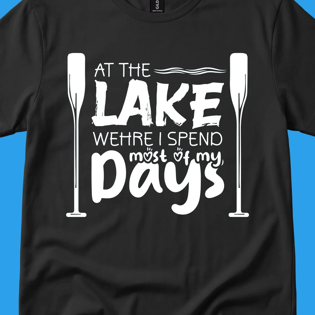 Text design "At The Lake Where I Spend Most Of My Days" with paddles and waves, lake-life-days concept.