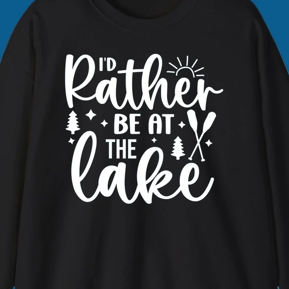 I'd Rather Be At The Lake typography design with sun rays, trees, and oars.