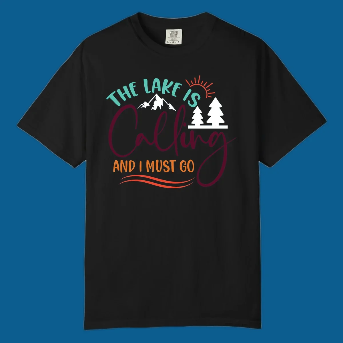 The Lake Is Calling And I Must Go nature graphic with mountains, trees, and sun rays.