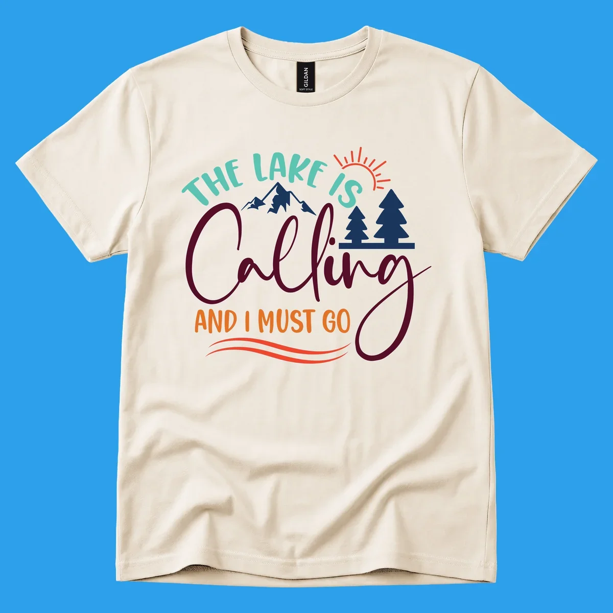 The Lake Is Calling And I Must Go nature graphic with mountains, trees, and sun rays.