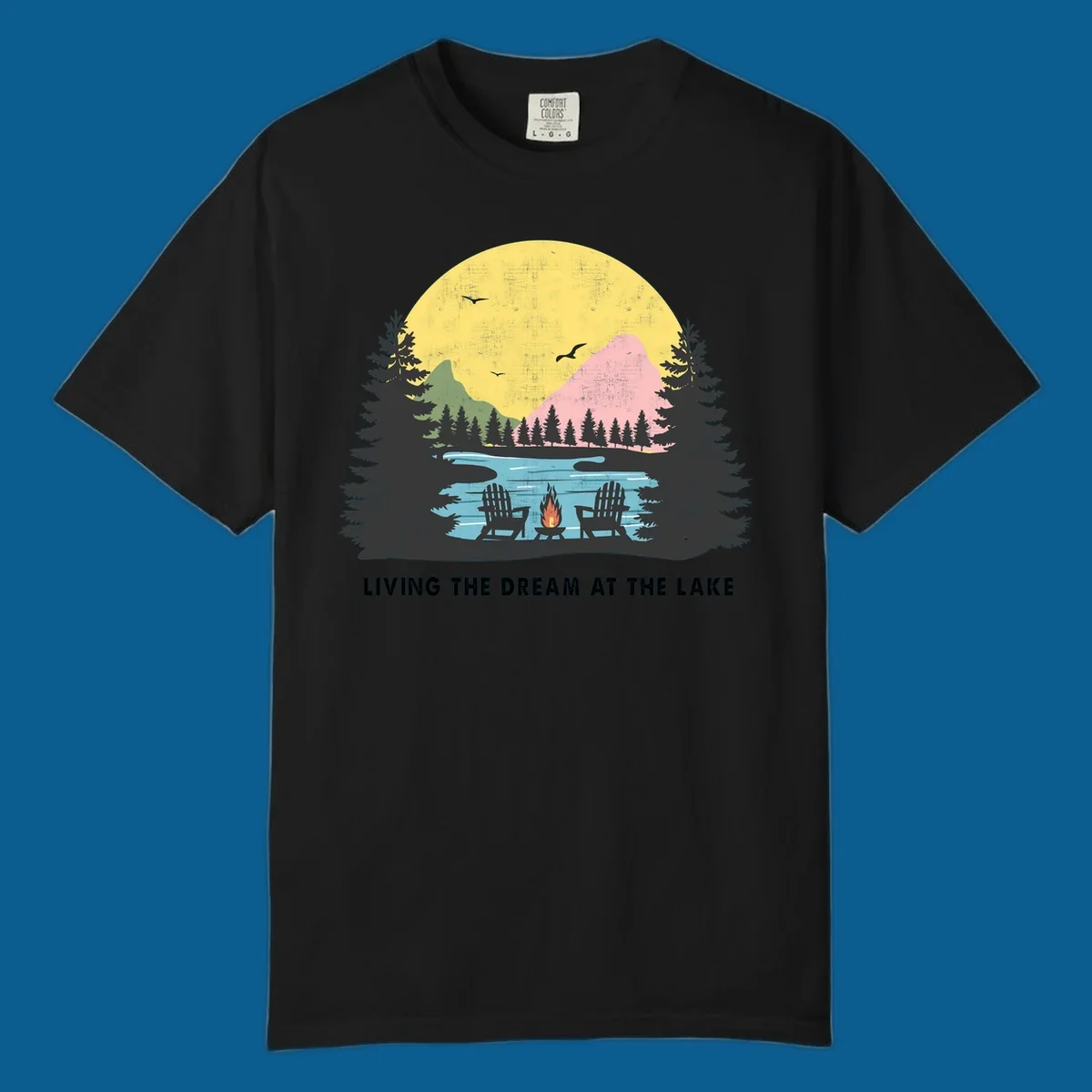 Lake life dream scene with Adirondack chairs, campfire, and sunset over mountains. Text: LIVING THE DREAM AT THE LAKE