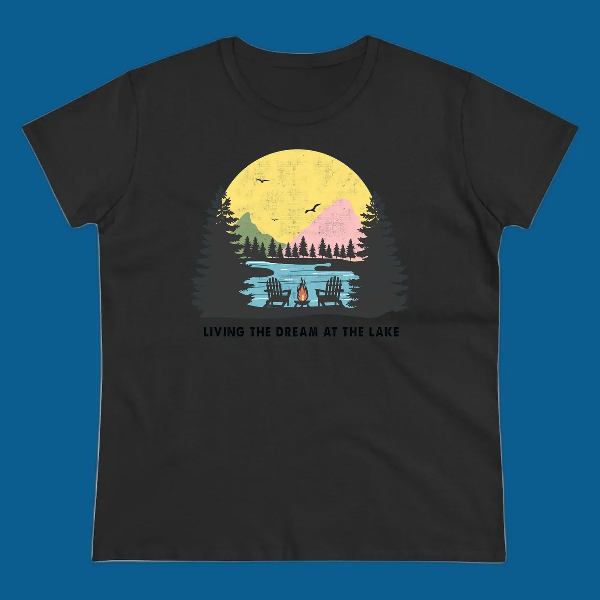 Lake life dream scene with Adirondack chairs, campfire, and sunset over mountains. Text: LIVING THE DREAM AT THE LAKE