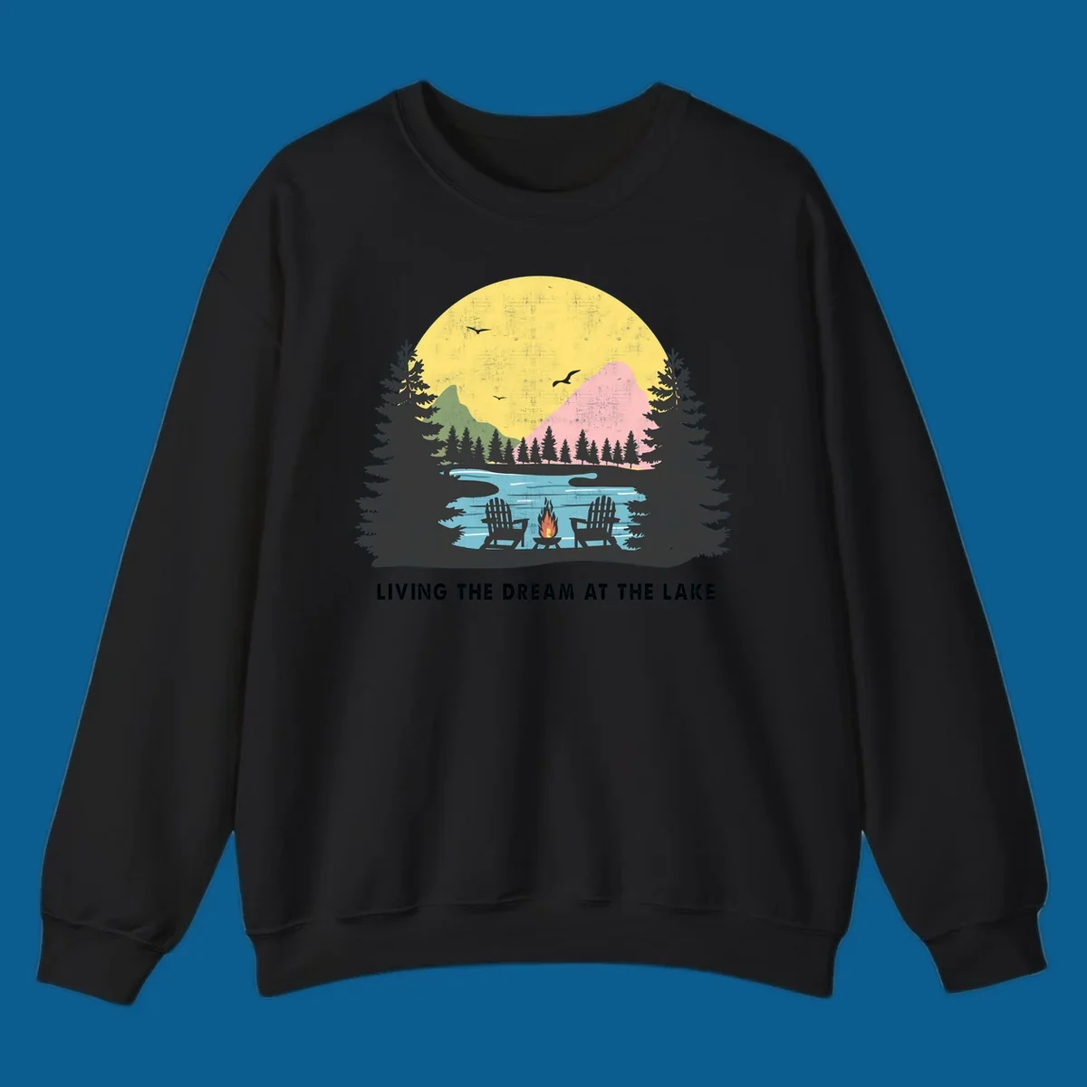 Lake life dream scene with Adirondack chairs, campfire, and sunset over mountains. Text: LIVING THE DREAM AT THE LAKE