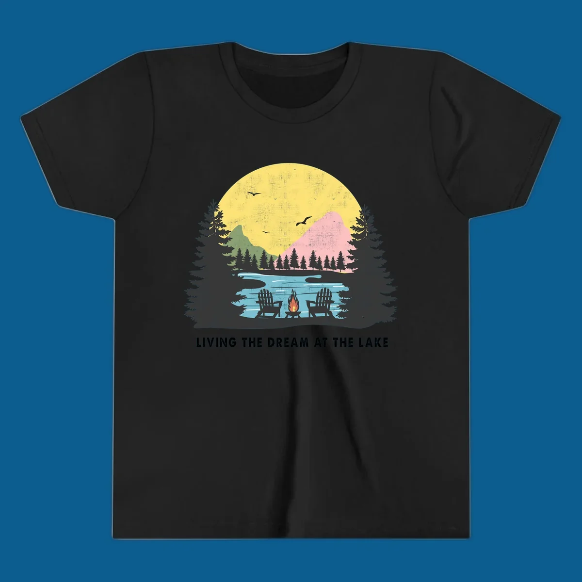 Lake life dream scene with Adirondack chairs, campfire, and sunset over mountains. Text: LIVING THE DREAM AT THE LAKE