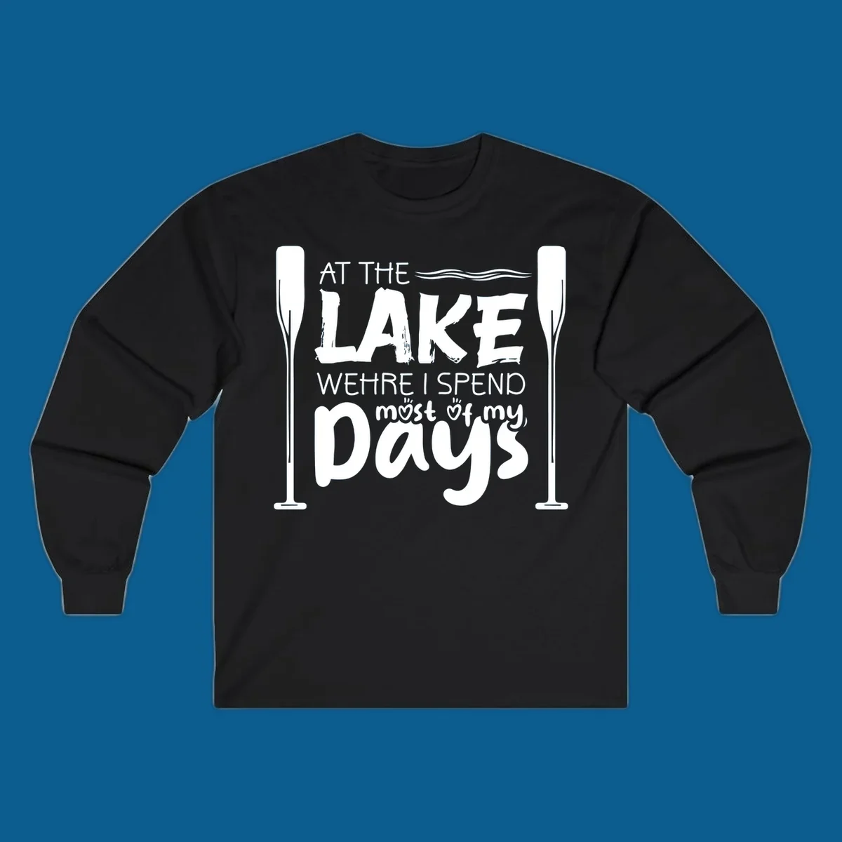 Text design "At The Lake Where I Spend Most Of My Days" with paddles and waves, lake-life-days concept.