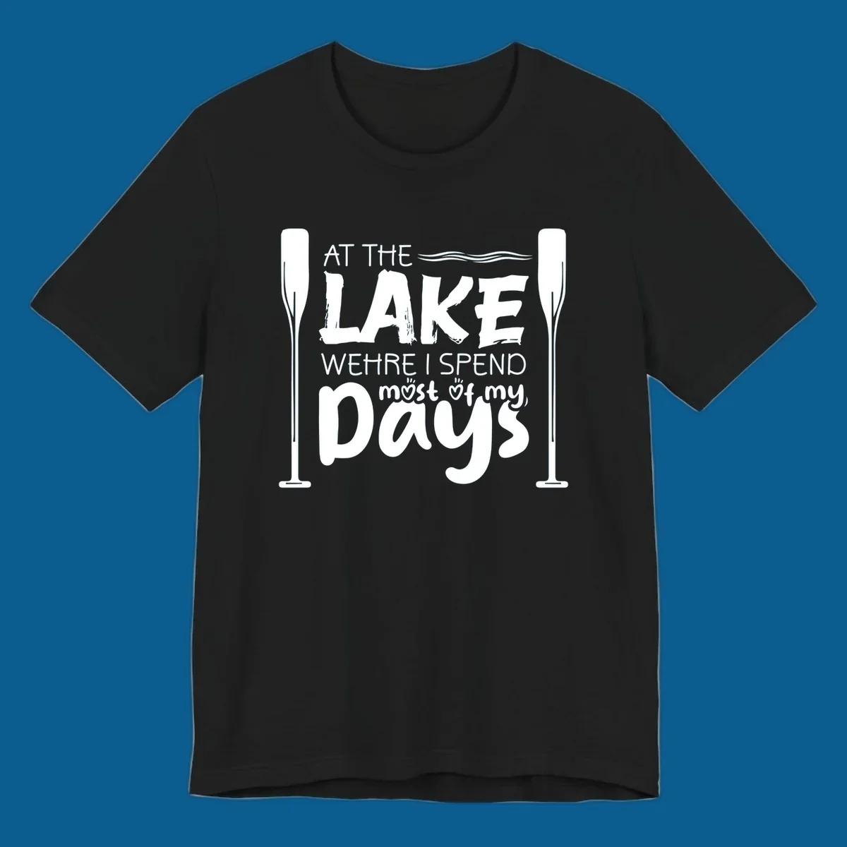 Text design "At The Lake Where I Spend Most Of My Days" with paddles and waves, lake-life-days concept.