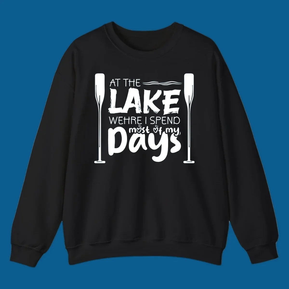 Text design "At The Lake Where I Spend Most Of My Days" with paddles and waves, lake-life-days concept.