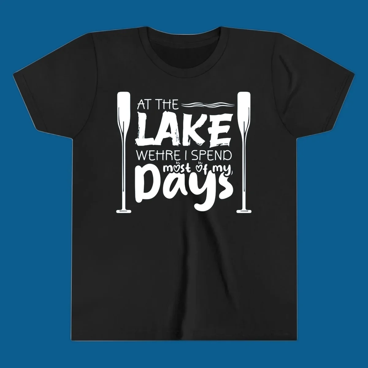 Text design "At The Lake Where I Spend Most Of My Days" with paddles and waves, lake-life-days concept.