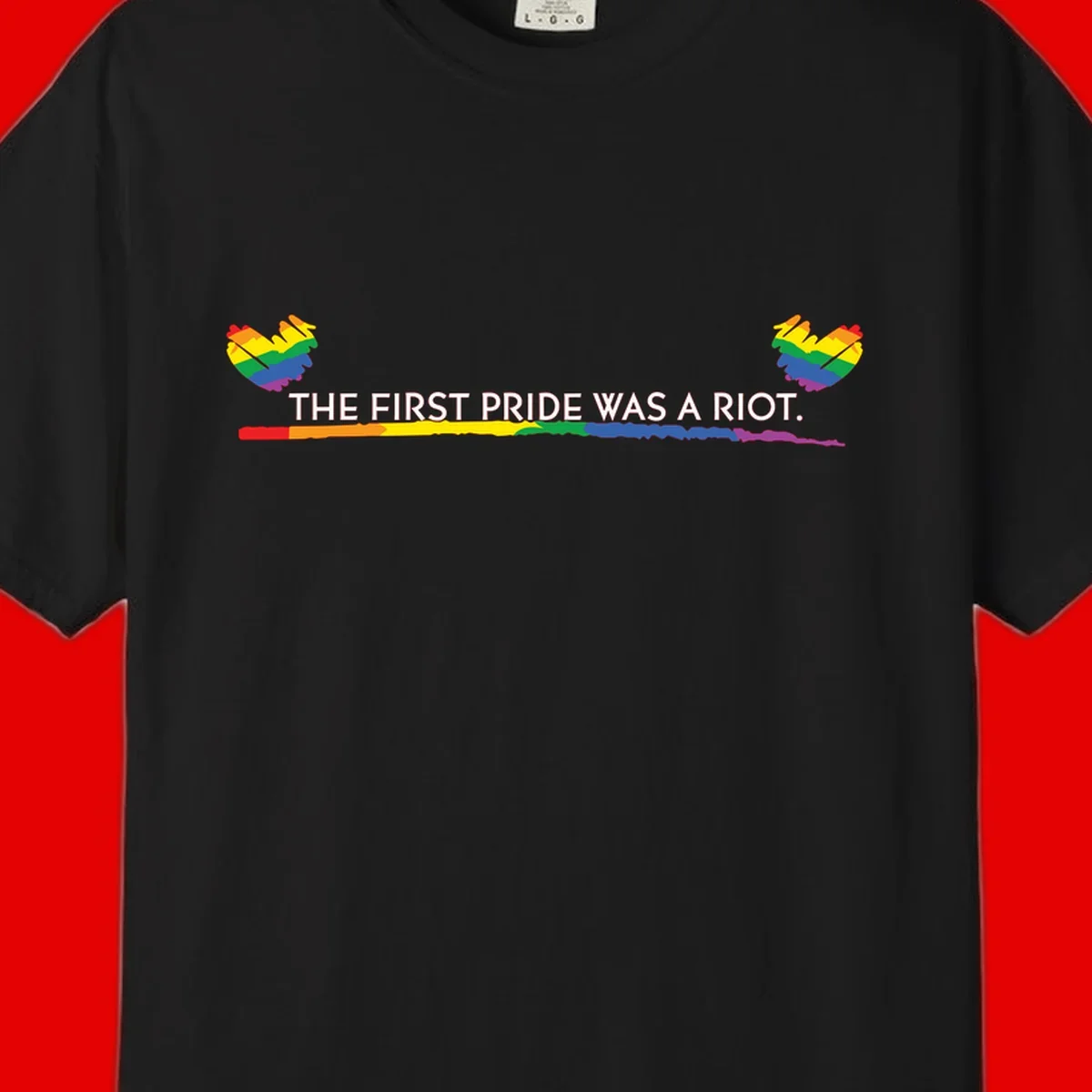 Gray background with white text reading 'THE FIRST PRIDE WAS A RIOT' surrounded by rainbow pride hearts and gradient stripe