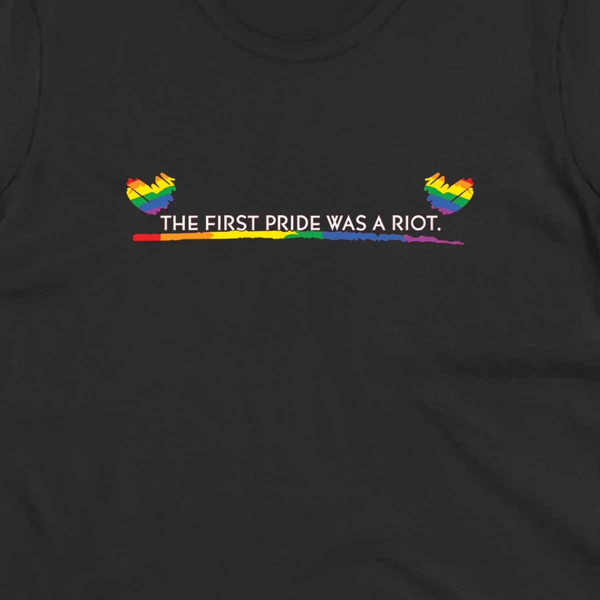 Gray background with white text reading 'THE FIRST PRIDE WAS A RIOT' surrounded by rainbow pride hearts and gradient stripe