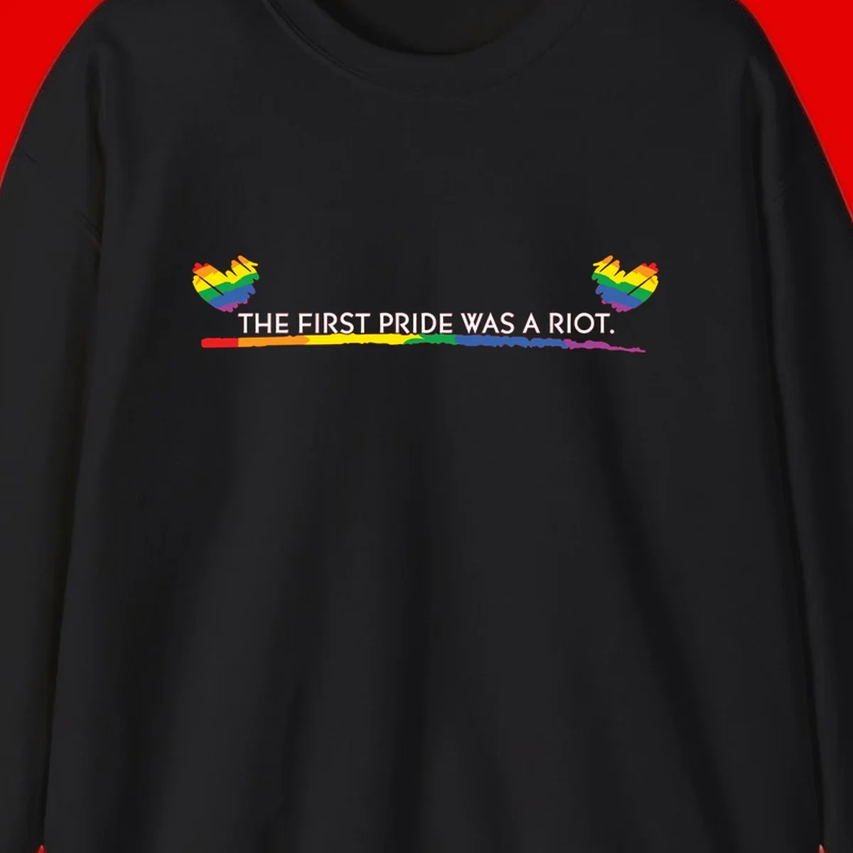 Gray background with white text reading 'THE FIRST PRIDE WAS A RIOT' surrounded by rainbow pride hearts and gradient stripe