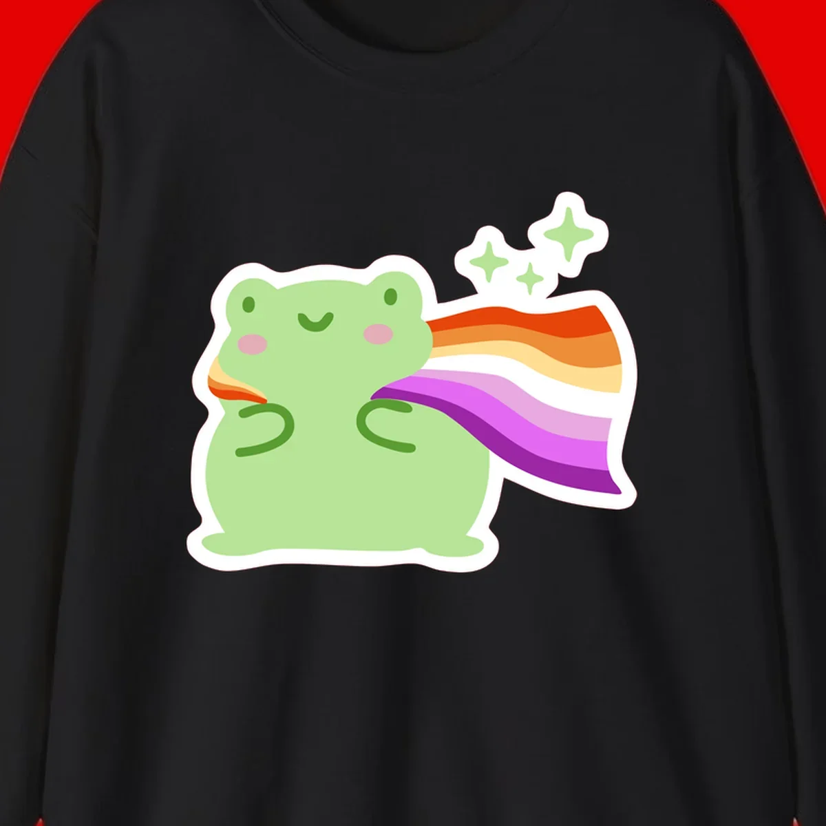 Cute green frog with pink cheeks wearing a rainbow pride cape, surrounded by sparkle stars